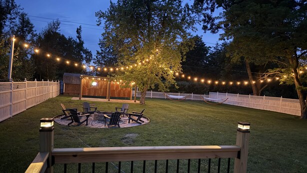 A backyard with a fire pit, outdoor seating, and string lights.