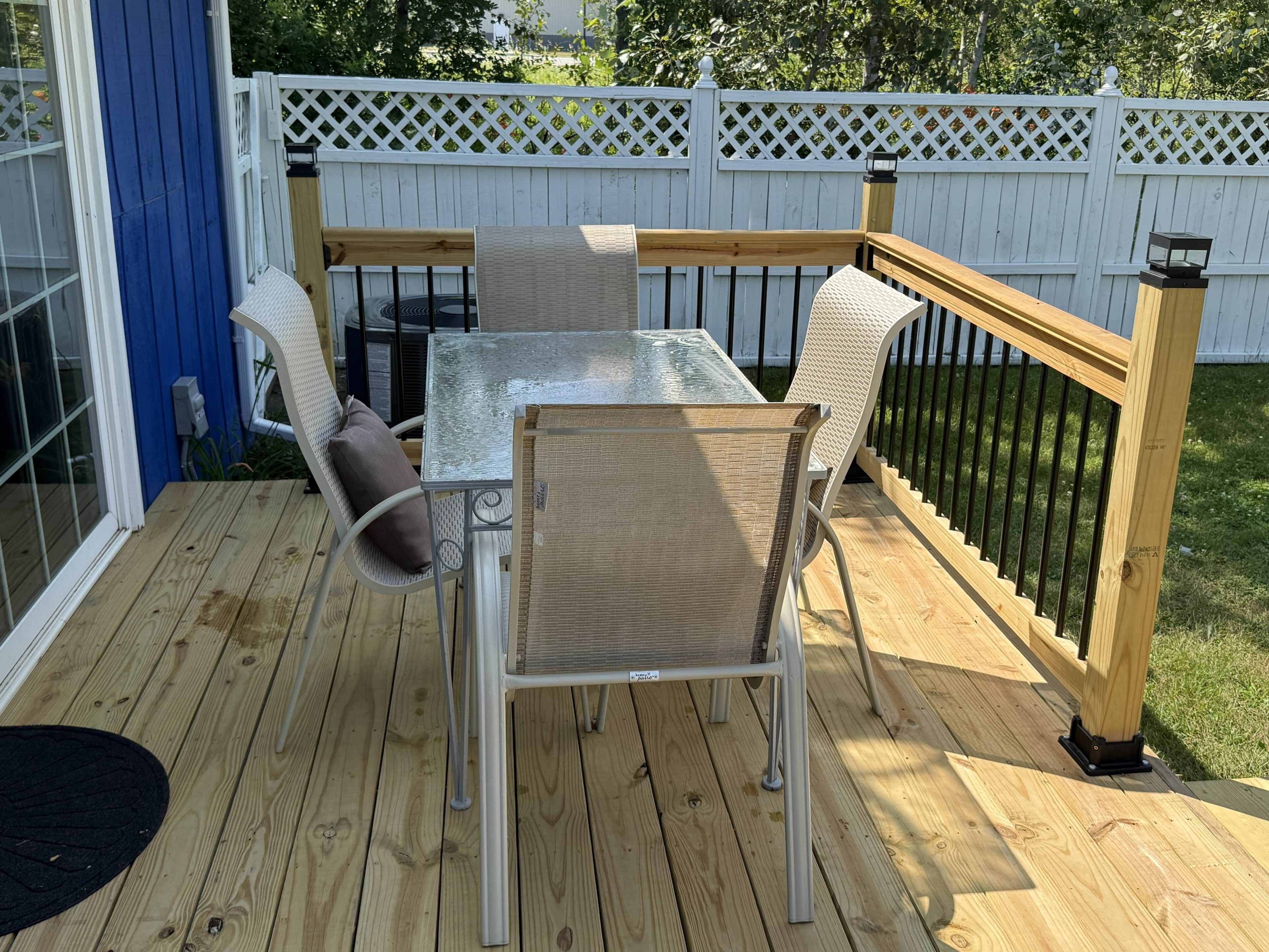 A deck with a table and chairs, a white fence, and a wooden railing.