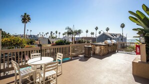 A patio with a round table and chairs, a barbecue grill, and a view of the ocean. - Come Stay at This Coastal Comfort in the Heart of Socal (Oceanside)