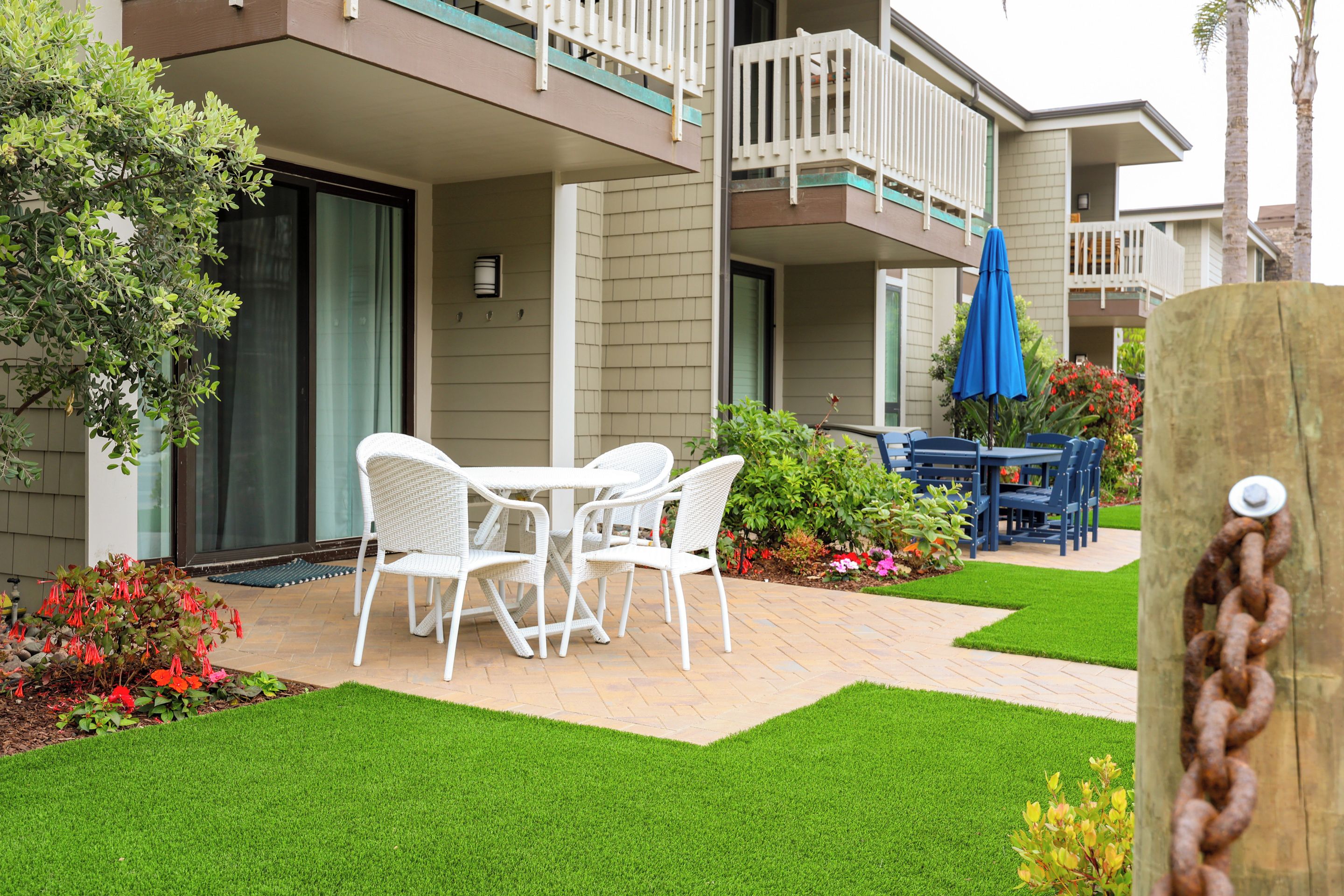 A courtyard with a patio table and chairs, surrounded by a well-maintained lawn and potted plants.