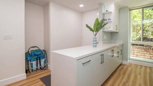 A modern kitchen with white cabinets, a blue-striped vase with a plant, and a window with a view of greenery. - Come Stay at This Coastal Comfort in the Heart of Socal (Oceanside)