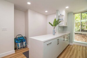 A modern kitchen with white cabinets, a blue-striped vase with a plant, and a window with a view of greenery. - Come Stay at This Coastal Comfort in the Heart of Socal (Oceanside)