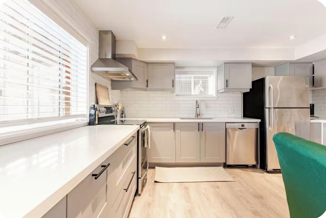 A modern kitchen with white cabinetry, a stainless steel refrigerator, and a window with blinds.