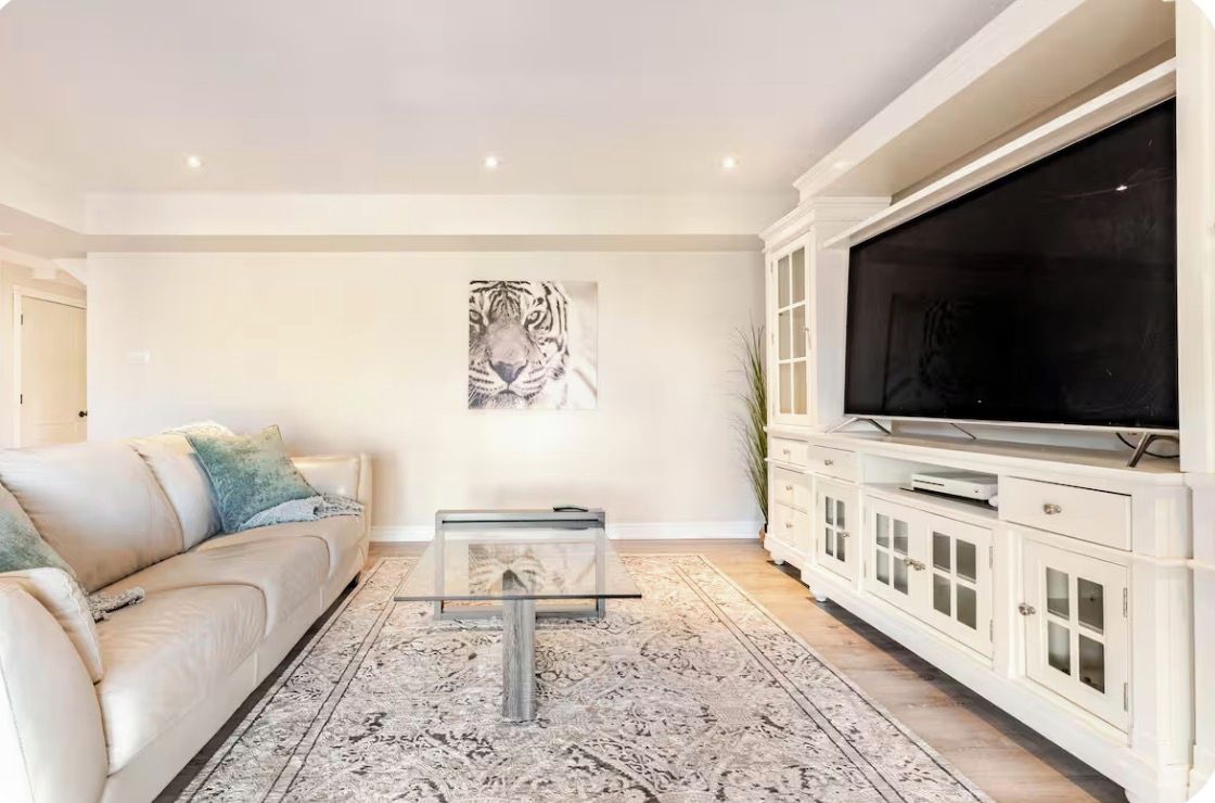 A living room with a sofa, a glass coffee table, a large flat-screen TV, a cabinet with drawers, and a tiger artwork on the wall.