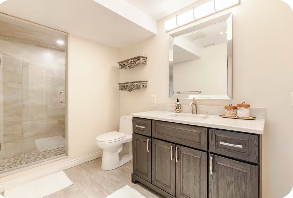 A bathroom with a glass-enclosed shower, a toilet, and a vanity with drawers and a mirror.
