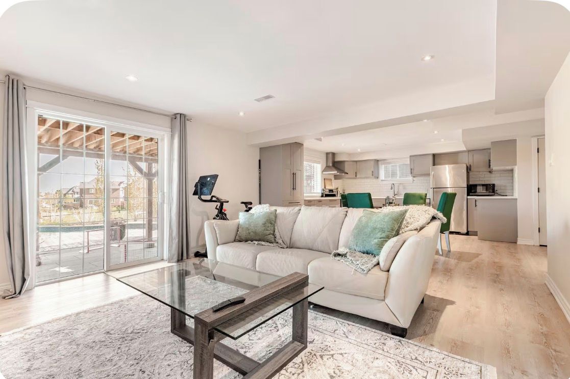 A modern living room with a glass coffee table, a sofa with cushions, and a view through a large sliding glass door to an outdoor area.
