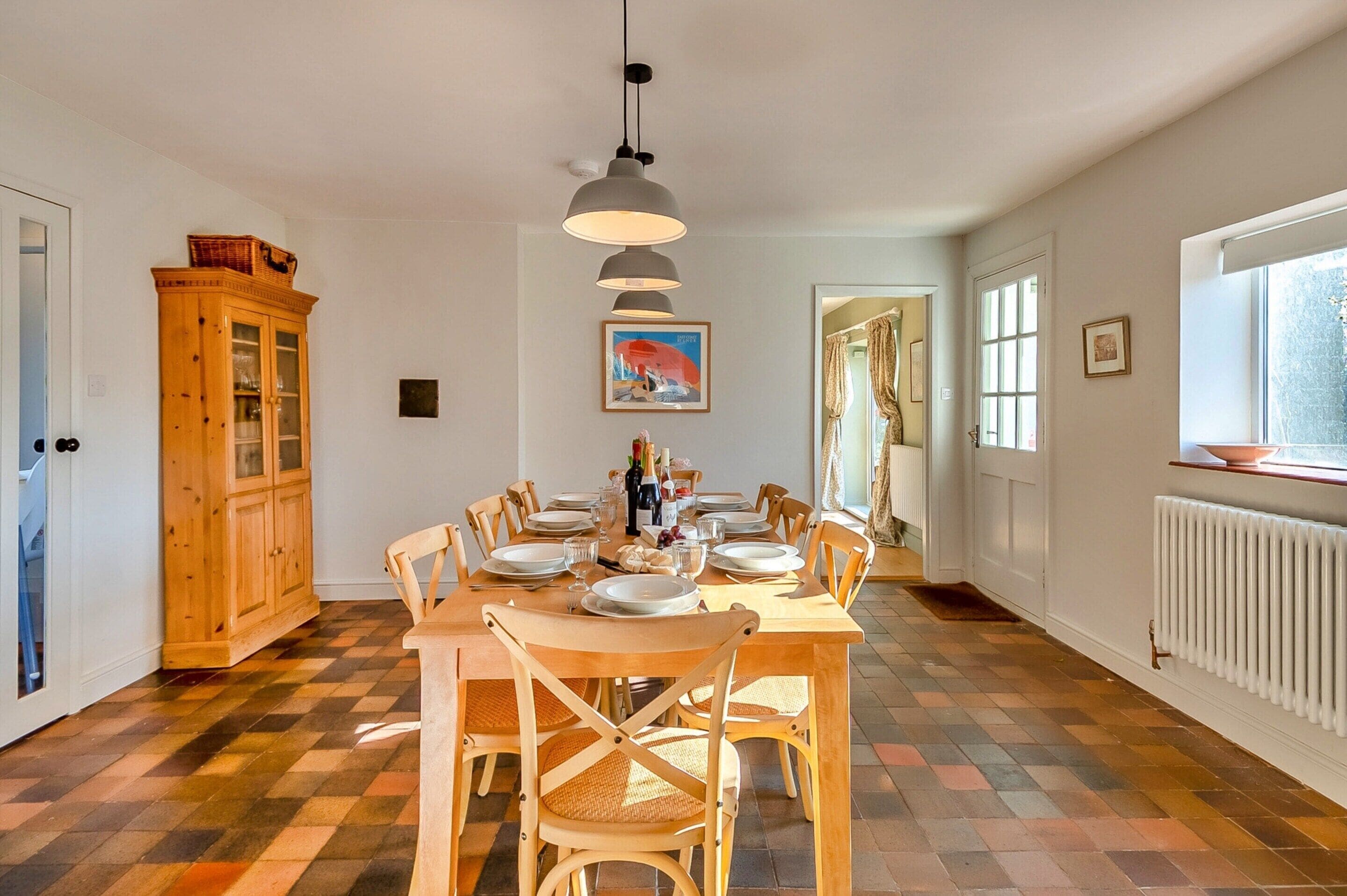A dining room with a checkered floor, wooden chairs, a table set for six, and a pendant light.