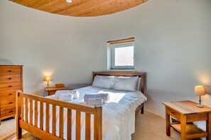 Ein Schlafzimmer mit einem hölzernen Bett, Nachttischen mit Lampen, einer Kommode und einem Fenster.