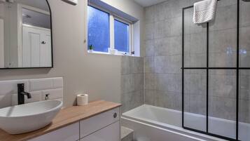 A modern bathroom with a white sink, a bathtub, and a shower area.