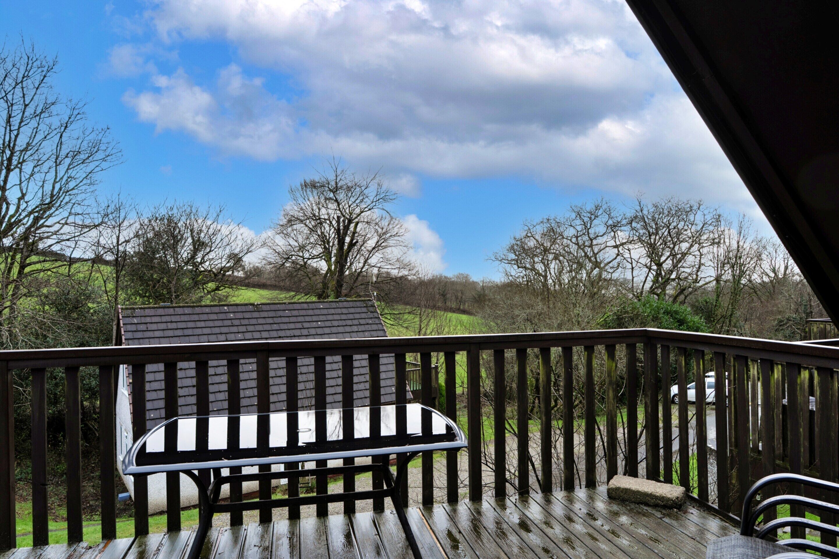 A wooden deck with a bench, a view of a green landscape, and a clear sky.