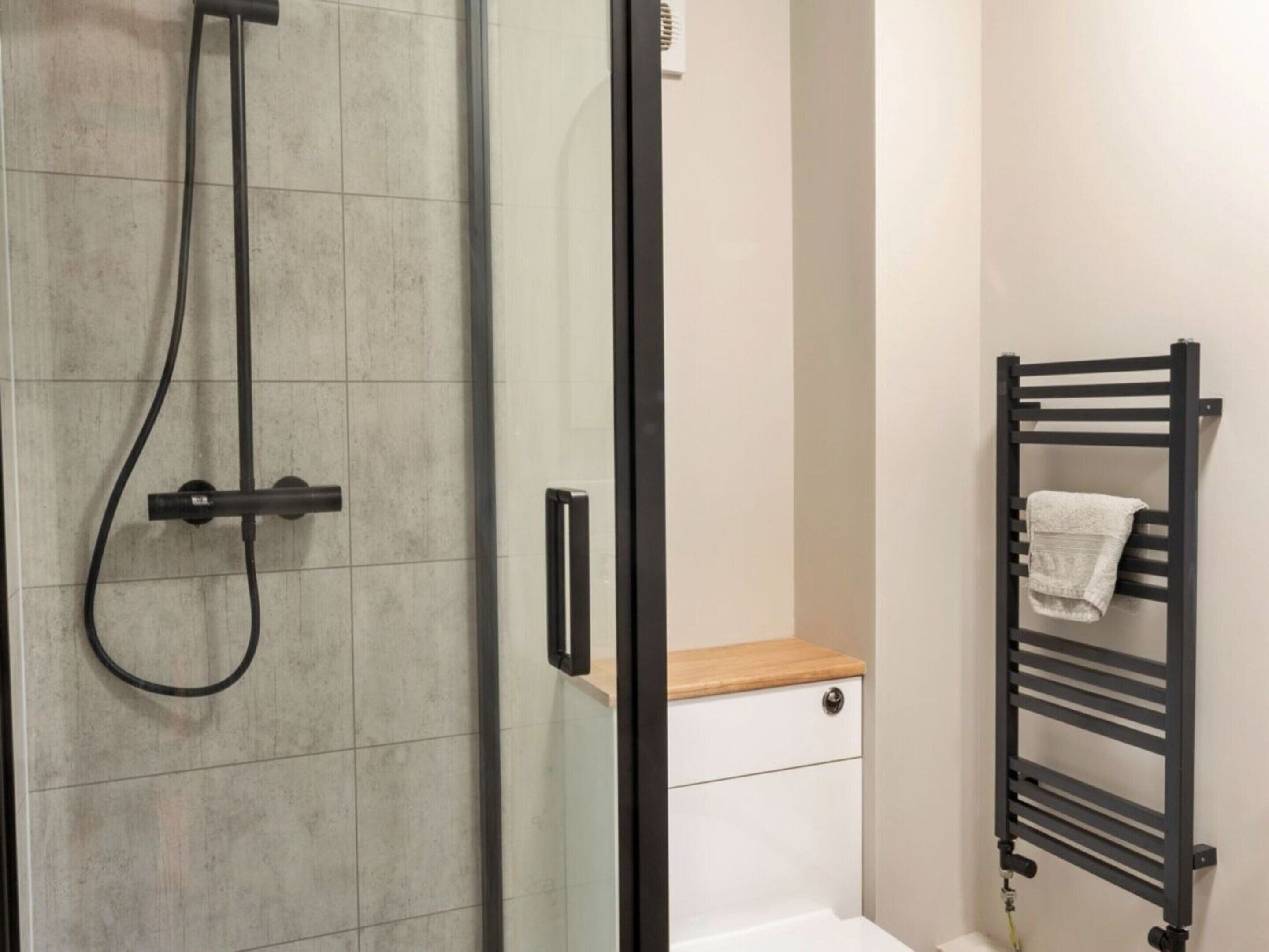 A bathroom with a glass shower enclosure, a white toilet, and a black towel rack.