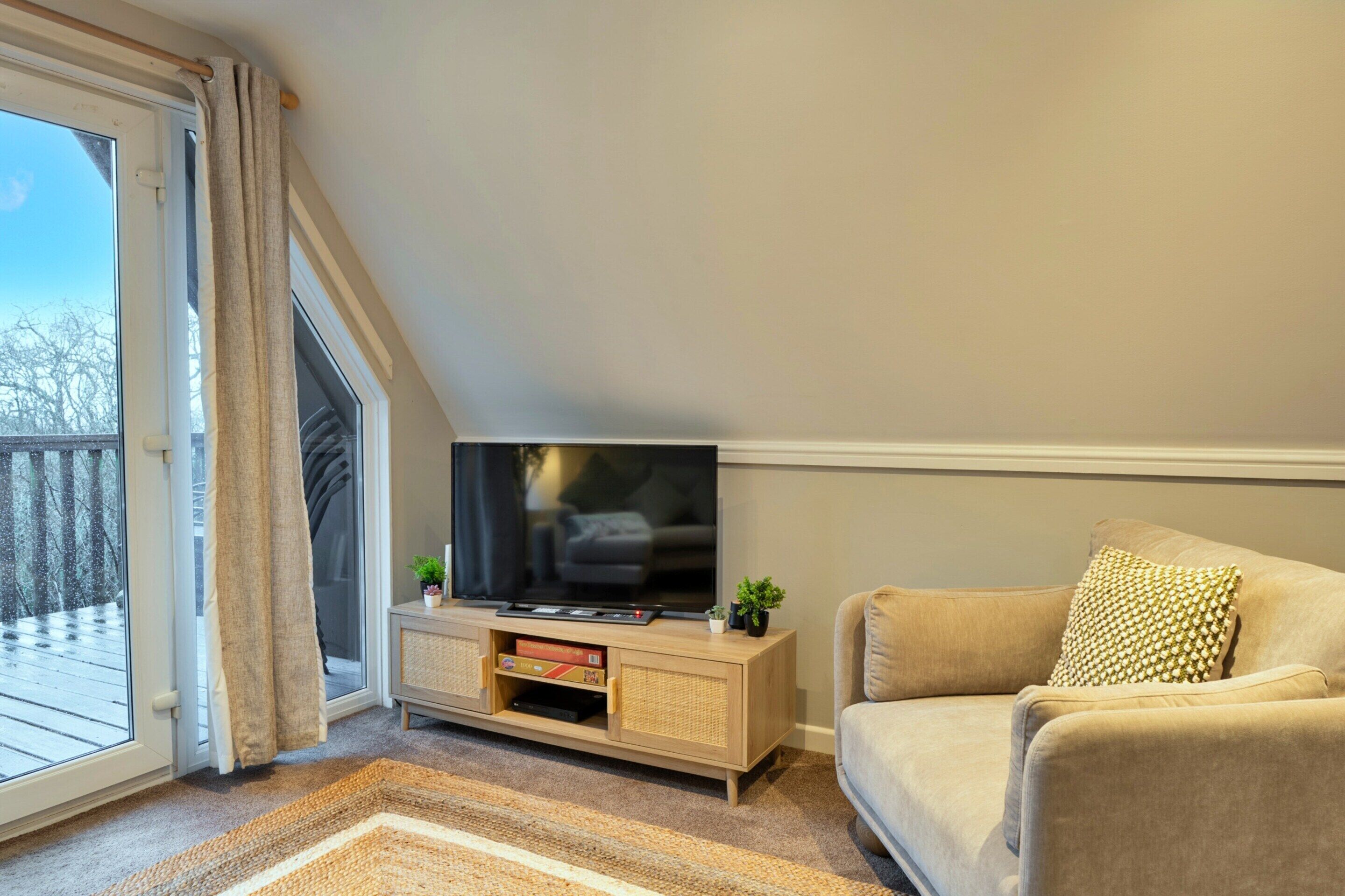 A living room with a television on a wooden stand, a sofa, and a view of a snowy deck through a glass door.