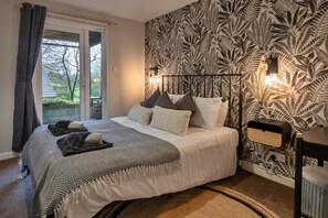 Un dormitorio con cama, almohadas, mesita de noche, lámpara y ventana con cortinas.