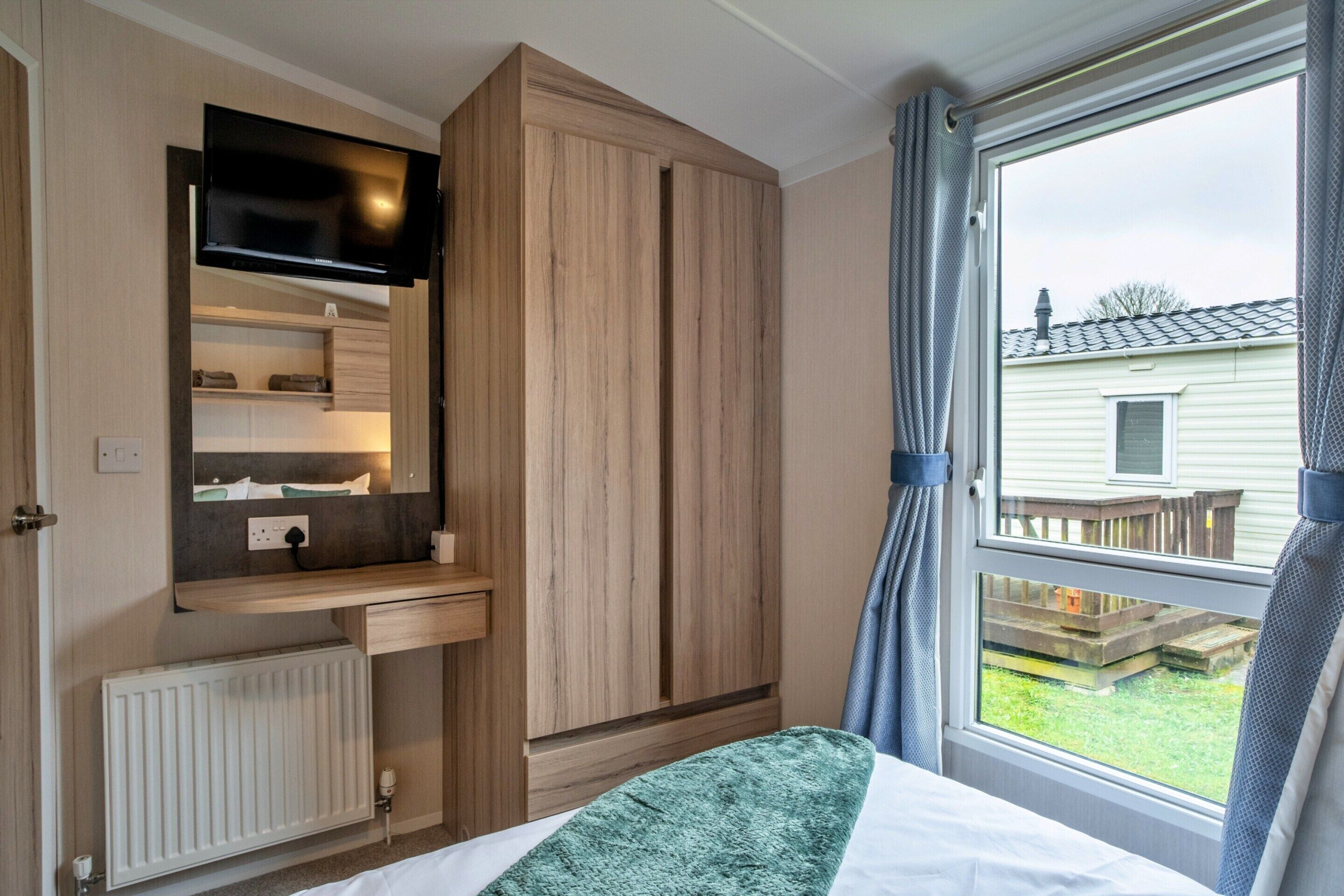 A bedroom with a bed, a built-in desk, a television, and a window with curtains.