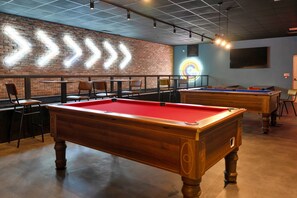 A pool table with a red felt surface, surrounded by chairs and tables in a room with brick walls and a ceiling with grid-like patterns. - Pine Forest Lodge in Cornwall (Newquay)