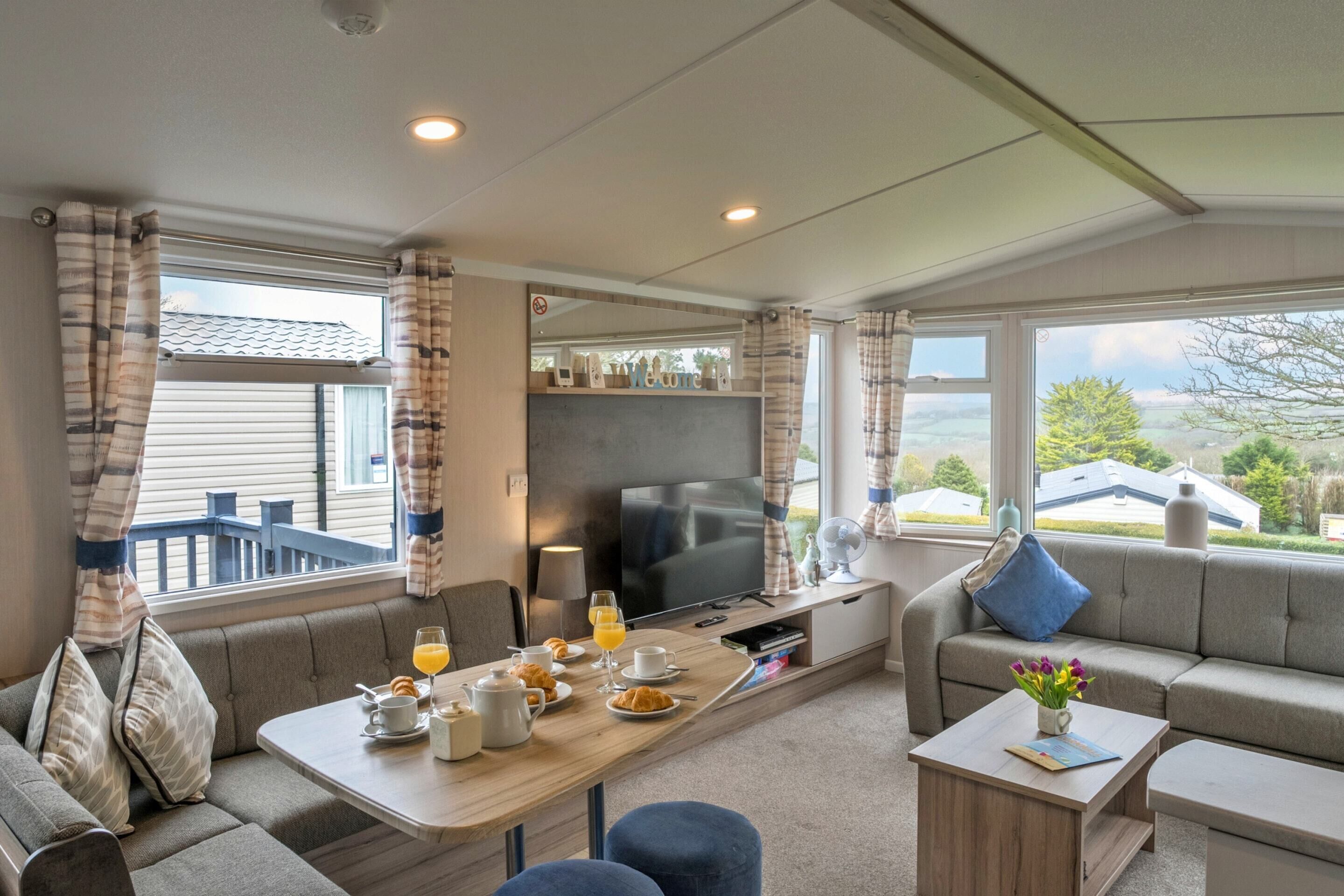A cozy living area with a sofa, a dining table set with breakfast items, a flat-screen TV, and a view of the outdoors.