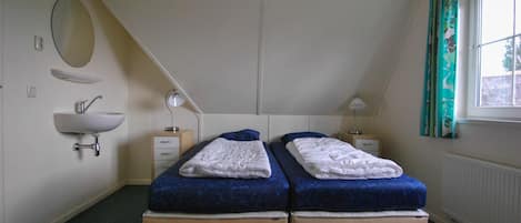Un dormitorio con dos camas, una mesita de noche, una lámpara, un espejo y una ventana con cortinas.