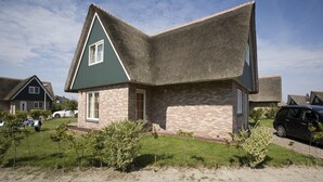 Une maison d’habitation avec un toit à forte pente, une façade en briques et une pelouse bien entretenue.