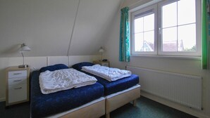 Une chambre avec deux lits simples, une fenêtre avec des rideaux, un radiateur et des lampes de chevet.