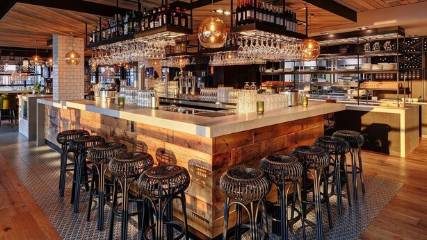 Un espace bar avec un plafond en bois, des tabourets de bar et des étagères remplies de bouteilles et de verres.
