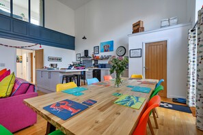 A modern kitchen with a central island, a dining area with colorful placemats, and a living space with a sofa and cushions. - Charming Chapel House Norfolk (Dereham)