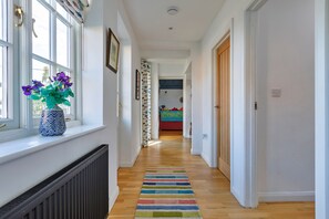 A hallway with a radiator, a window with a vase of flowers, and a colorful striped rug. - Charming Chapel House Norfolk (Dereham)