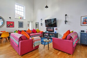 A living room with two red sofas, colorful cushions, a flat-screen TV, a wooden coffee table, and a bookshelf. - Charming Chapel House Norfolk (Dereham)