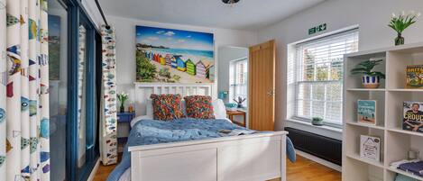 Un dormitorio con cama, un cuadro, una estantería y una ventana.