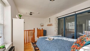 Ein Schlafzimmer mit Bett, Schminktisch, Spiegel, Fenster mit Jalousien und Deckenventilator.