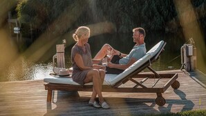 A couple sitting on a wooden lounge chair by a body of water with a wooden deck and a metal railing. - Elegant Waterfront Bungalow With Jetty (Makkum)