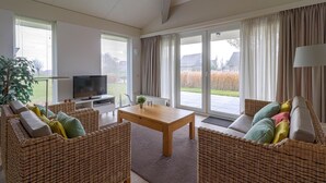 A spacious living room with a television, wicker furniture, a wooden coffee table, and large windows with curtains. - Elegant Waterfront Bungalow With Jetty (Makkum)