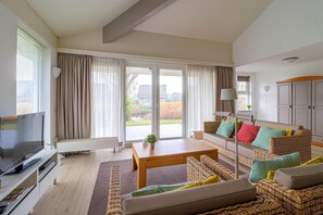 A modern living room with a television, sofa, and a view of the outdoors through large windows. - Elegant Waterfront Bungalow With Jetty (Makkum)
