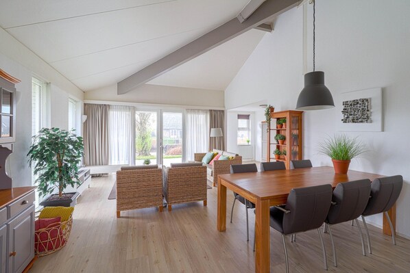 A spacious living area with a dining table, chairs, a sofa, and a large window. - Elegant Waterfront Bungalow With Jetty (Makkum)
