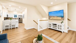 A spacious living area with a large flat-screen TV, wooden flooring, a dining area with white furniture, and a kitchen with modern appliances. - Spacious 4-bedroom townhome in fabulous Ocean City with AC (Ocean City)