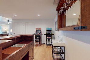 Una cocina compacta con encimera de madera, un fregadero y dos máquinas de videojuegos.