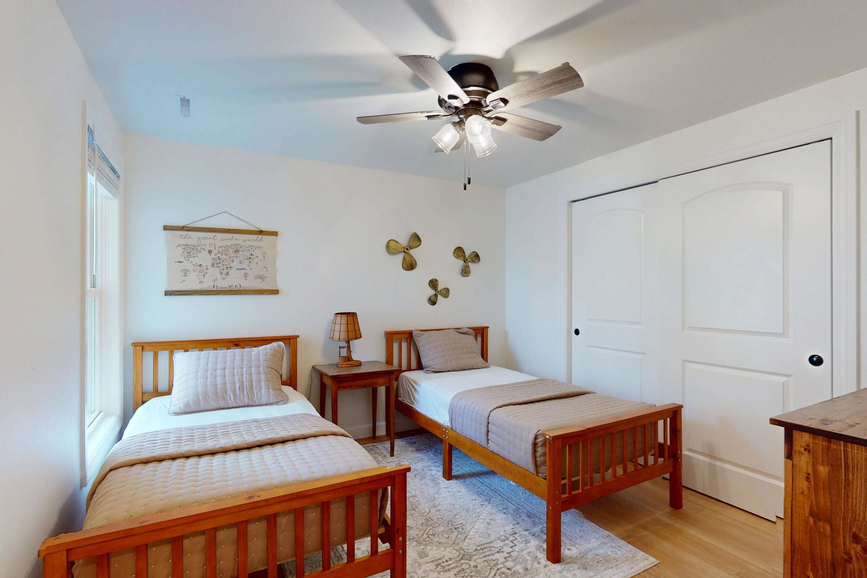 Une chambre à coucher avec deux lits en bois, un ventilateur de plafond, une porte et une lampe fixée au mur.