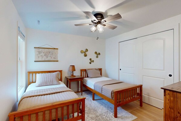 A bedroom with two wooden beds, a ceiling fan, a door, and a wall-mounted lamp.