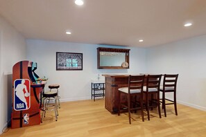 A dining area with a wooden table and chairs, a bar area with a sink, and a basketball arcade game.