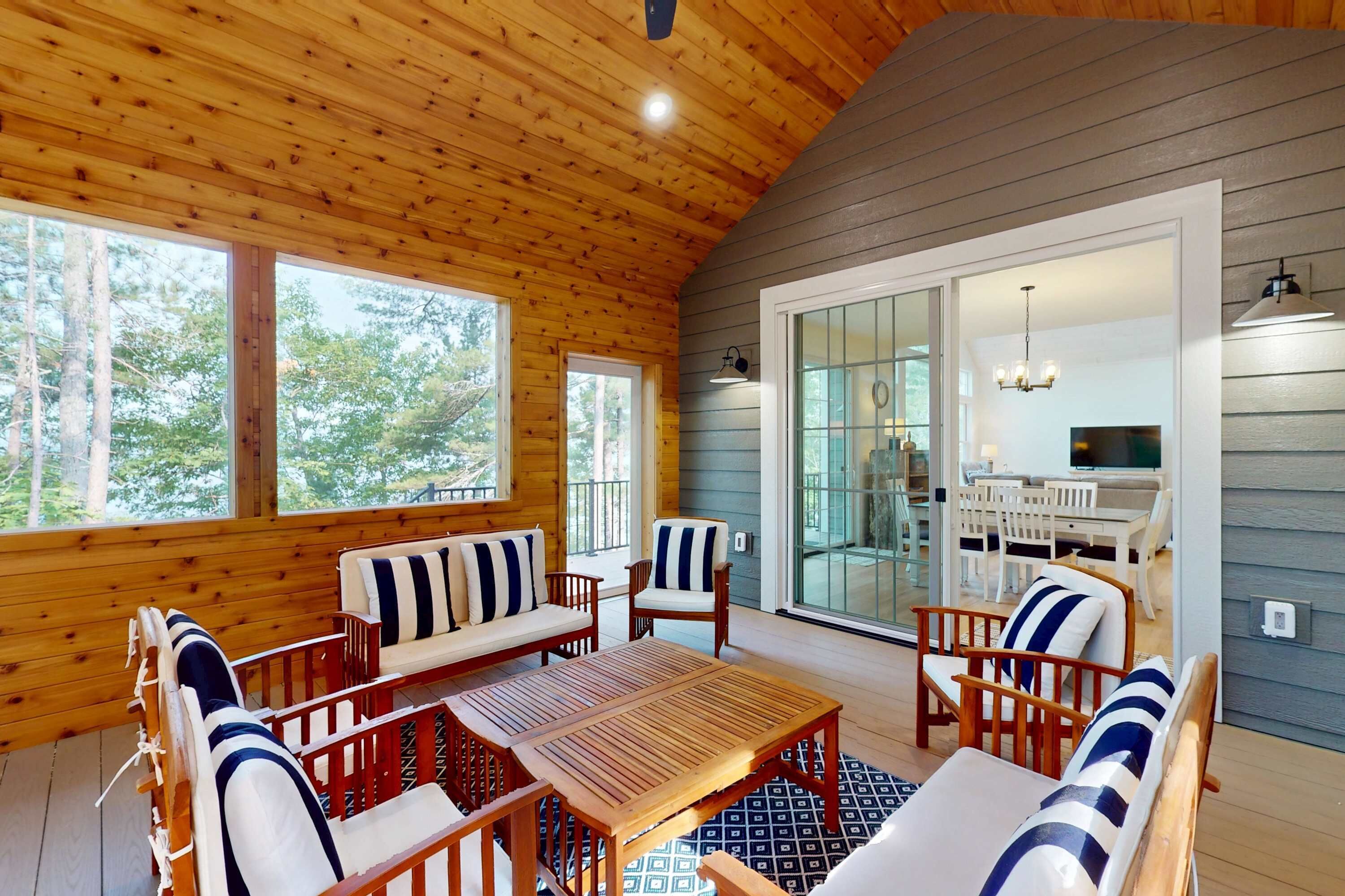 Un interior de madera con comedor, sofás y vistas a un patio exterior a través de un ventanal.