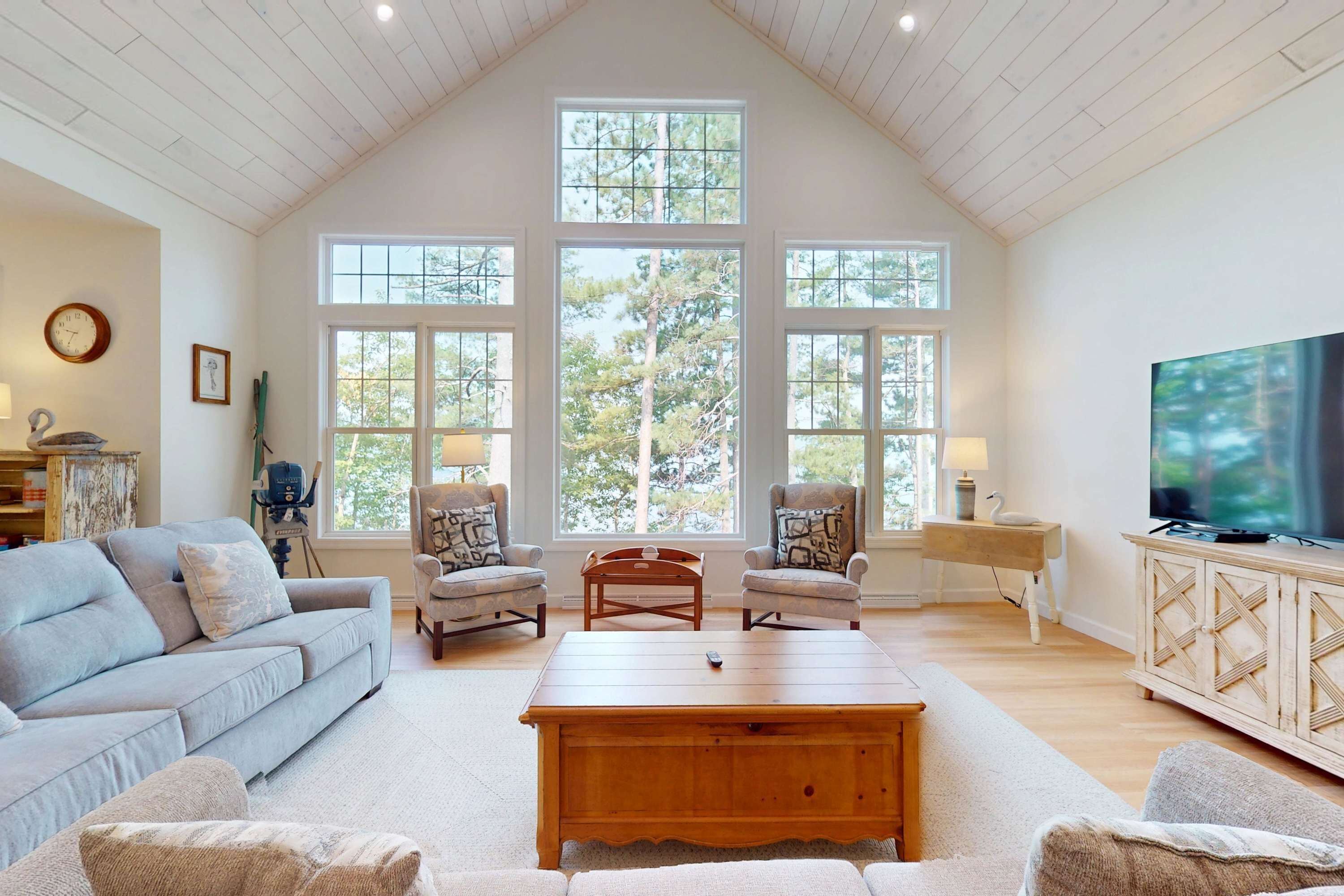 A spacious living room with a high ceiling, large windows, a television, and a cozy seating area.