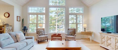 A spacious living room with a high ceiling, large windows, a television, and a cozy seating area.