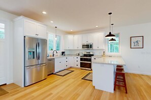 Cocina moderna con armarios blancos, electrodomésticos de acero inoxidable y suelo de madera.