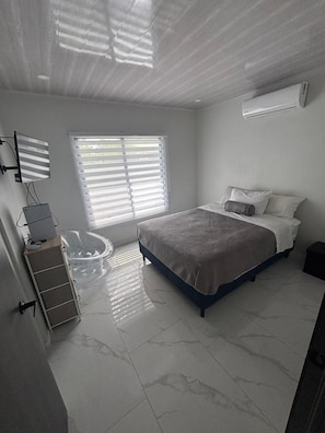 A bedroom with a bed, a window with blinds, a wall-mounted air conditioner, and a clear glass fishbowl. - Beautiful 3-bedroom house with AC in charming Puntarenas Province (Uvita)