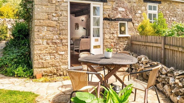 A stone house with a patio, a round table, wicker chairs, and a small garden. - Holiday Cottage Near Axminster (Axminster)