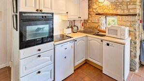 A compact kitchen with white cabinetry, a built-in oven, a microwave, and a dishwasher. - Holiday Cottage Near Axminster (Axminster)