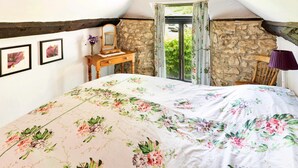 A bedroom with a sloped ceiling, stone walls, a wooden bed frame, a nightstand, and a window with curtains. - Holiday Cottage Near Axminster (Axminster)