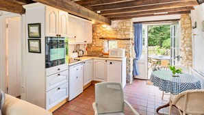 A compact kitchen with white cabinets, a built-in oven, and a stone wall. - Holiday Cottage Near Axminster (Axminster)
