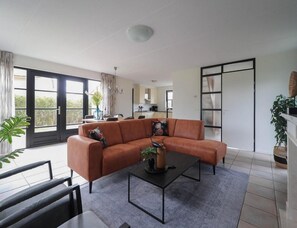 Un salon moderne avec un canapé d’angle, une table basse et une vue sur la cuisine grâce à une porte ouverte.