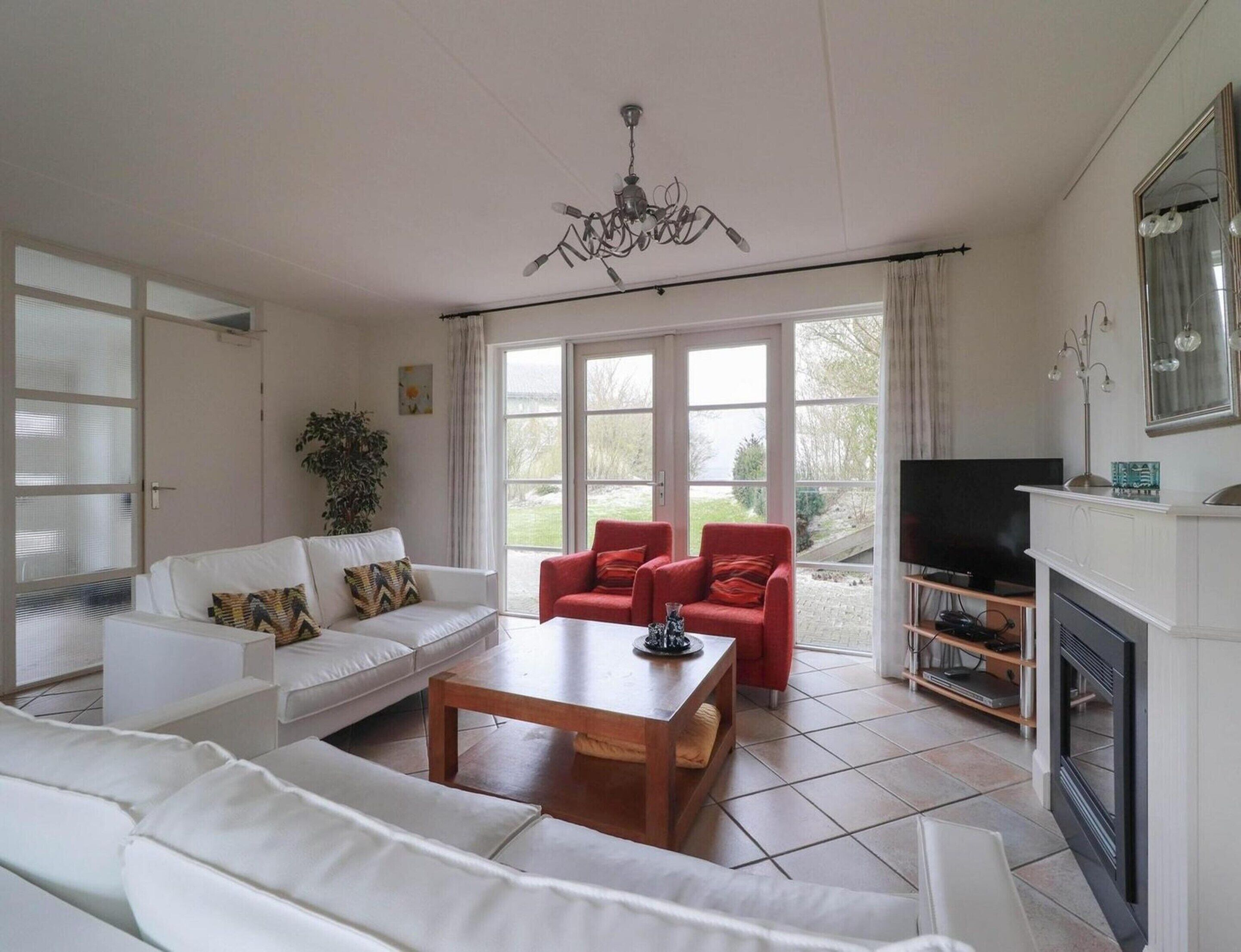 Ein Wohnzimmer mit einem weißen Sofa, roten Sesseln, einem Holztisch, einem Fernseher und einem Kamin.