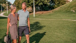 Ett par promenerar på en gräsbevuxen stig med träd och en byggnad i bakgrunden.